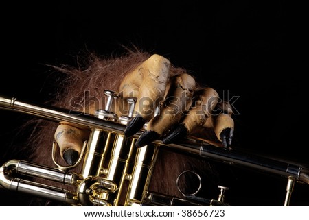 A gold brass Halloween trumpet with a monster hand against a black background.