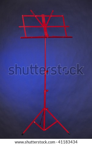 A red folding music stand isolated against a spotlight blue background in the vertical format.