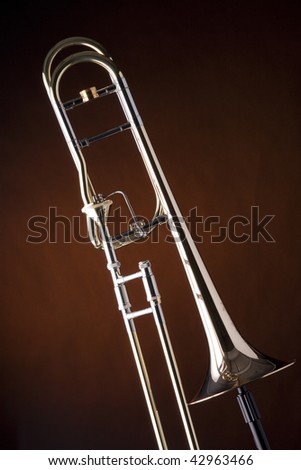 A professional gold trigger trombone isolated against a spotlight yellow gold background.