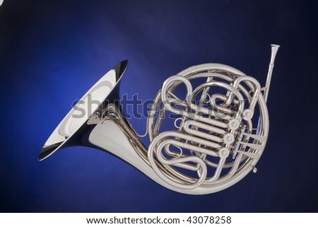 A professional silver French horn isolated against a spotlight blue background.