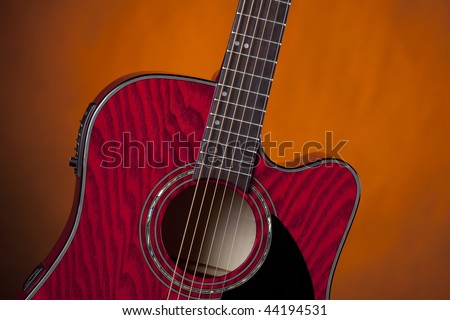 An acoustic electric guitar music instrument isolated against a dark spotlight gold or yellow background.