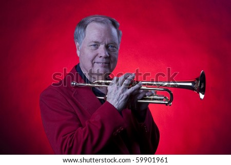 A gold colored brass trumpet being held close to face  by a trumpet player in the horizontal format with copy space and a red background.