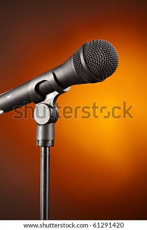 A microphone on a stand isolated against a spotlight gold background.