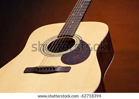 An acoustic guitar with a natural wood finish isolated on a spotlight gold background.
