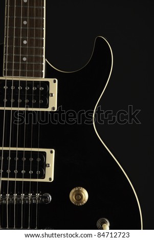 A black electric guitar isolated against a black background