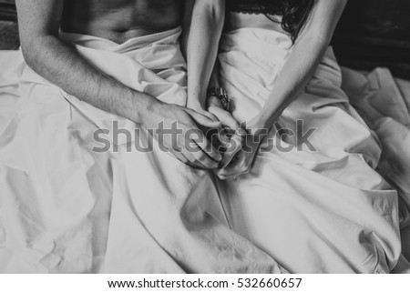 Man and woman in the sheets on the bed. Hands close-up.