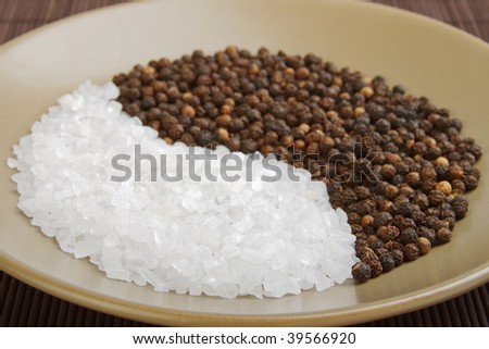 Coarse salt crystals and whole black peppercorns arranged in an eastern design, shallow DOF on the front edge of the spices