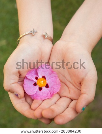 little girls hands holding a pink flower gently in her hands wearing a cross bracelet