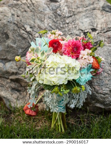 bright and beautiful bridal bouquet of flowers sitting on the grass and leaning against a rock