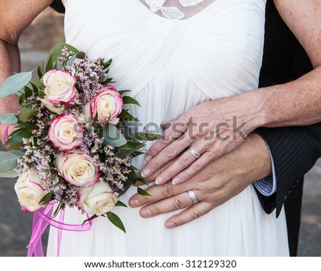 older bride and groom hands and rings with flowers