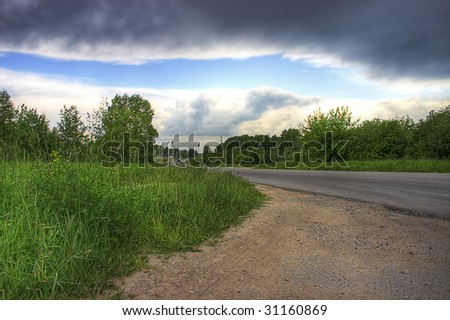 Landscape with a green grass and the asphalted road, on thunder-storm eve