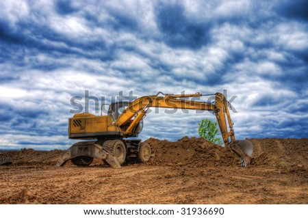 Old dredge digging the earth, photographed against the earth, the blue sky and a green bush