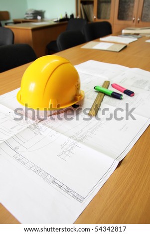 Desk, with the drawing laying on it, a helmet, a ruler and two felt-tip pens