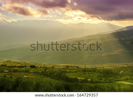 Rural landscape with green hills, mountains and sun rays