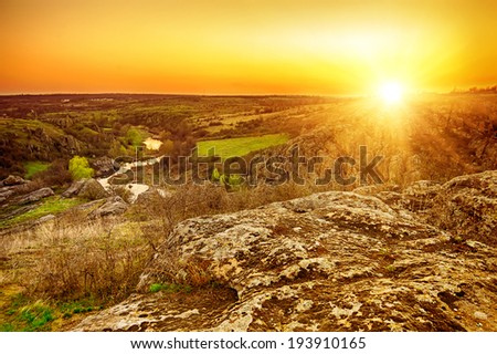 Rural sunset landscape with green hills, sun river and rocky mountains