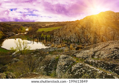 Rural sunset landscape with green hills, lake and sun rays