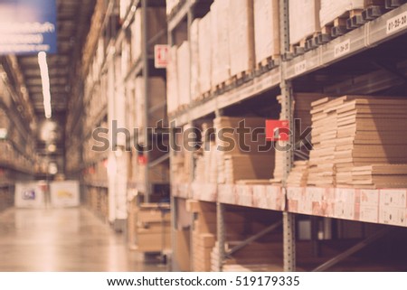 Blurred boxes on rows of shelves in warm light warehouse background.