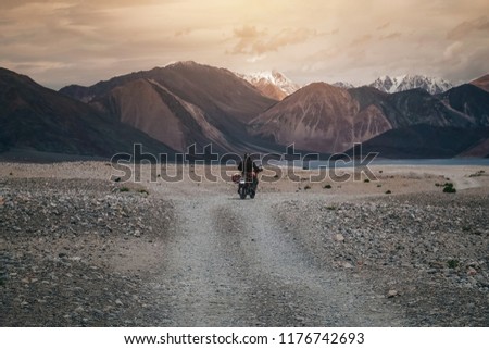 Tourist riding an adventure motorcycle on tuff and bumpy road on rock mountain in sunset lightning to explore the world, with copy space
