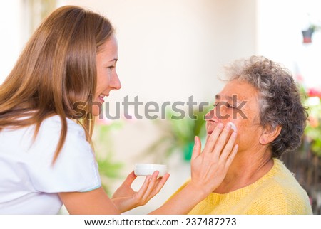 Caregiver rubs the face cream on the elderly womans face