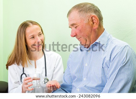 Young doctor helping the elderly man to take the pills