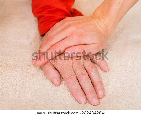 Elderly womans hand protected by young carer hand