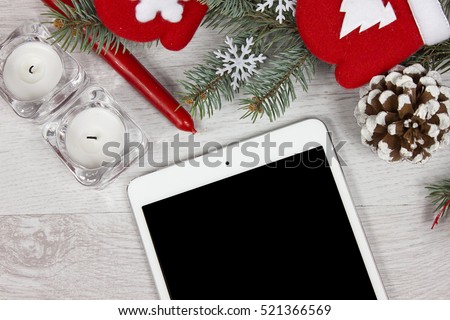Christmas decoration with red candle, red gloves, branch of pine and pine cone on white wood background with tablet mini
