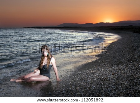 Bather sits on the shore of the sea during sunset