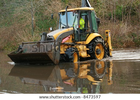 Bright yellow backhoe being driven in flood water