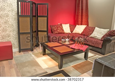 Modern and stylish dining room with sofa and table. Luxurious cushions. Red toned walls and dressing screen.