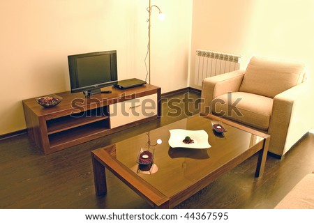 Living room with cosy sofa and arm chair, small table and DVD and TV set.