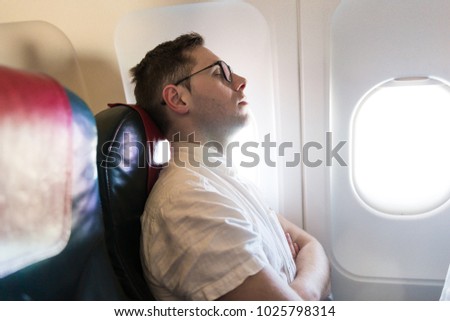 Side view of the elegant young man who is sitting on the plane near the window and sleeping