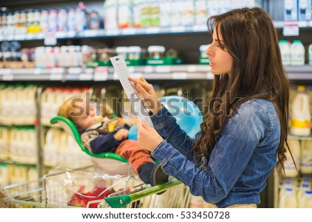 Young woman with a long shopping list in. Little son sleeping in shop