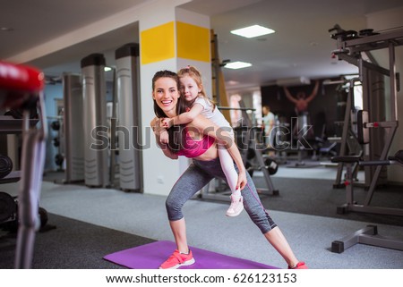 Sports older sister keeps on back her little sister and do exercise together, at the gym