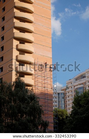 migrant workers in overalls with insurance work on scaffolding. Construction of monolithic brick house. Moscow, July 2015.