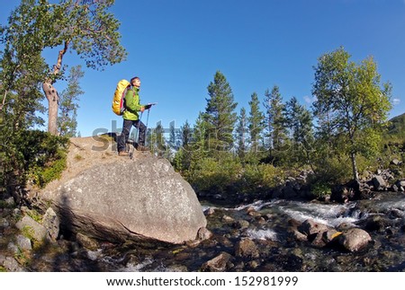 Hiker near mountain river with backpack, map and trekking poles