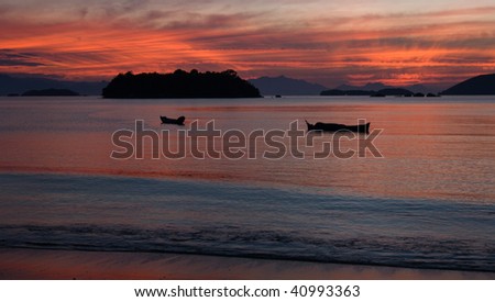Sun sets over islands in the sea in Paraty, east coast of Brazil while boats float in the bay