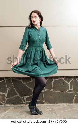 Young female model posing outdoor while pulling her green dress up