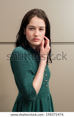 Young female model with a natural look touching her face. The background is a metal wall