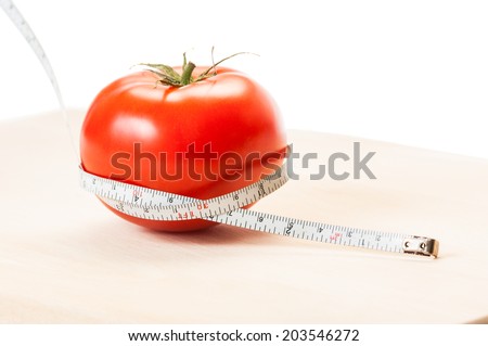 Measure calories of a perfect red tomato with a centimeter. Diet concept made of tomato, meter, wooden board and white background.