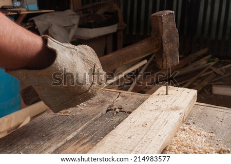 Male carpenter using a big hammer hitting a nail on wood in his workshop
