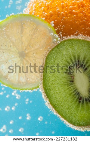 Fruits like orange, kiwi and lime in water with bubbles closeup