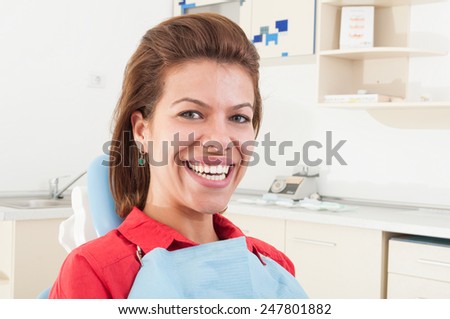 Female patient with big white teeth smiling and sitting in dentist chair