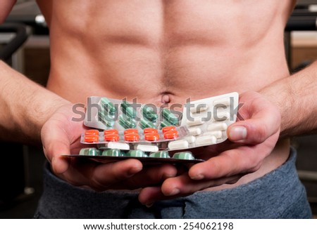 Muscle man holding bunch of blisters with colored vitamin pills
