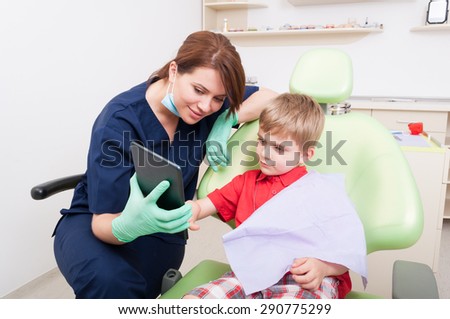 Smart and modern female dentist using tablet to relax kid or child patient