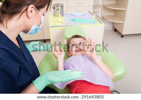 Dentist doctor calming scared kid patient in dental office. No fear of dentist concept