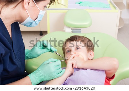 Scared kid with toothache in dentist office covering mouth
