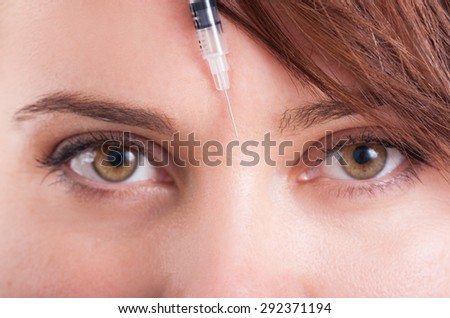 Botox syringe needle between eyes on forehead. Closeup view.
