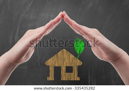Hands protecting green energy house concept draw on blackboard or school chalkboard