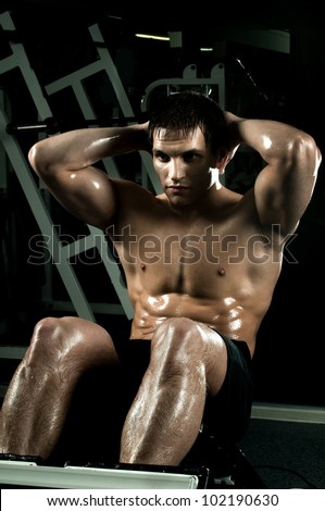 very power athletic guy ,  execute exercise on muscles belly, in  dark sport-hall