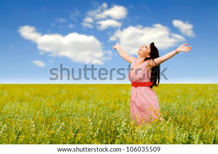 The young women  in a field with yellow colors, has lifted hands upwards, eyes are closed, smiles